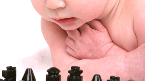 baby looking over a chess board appearing to get ready to play black
